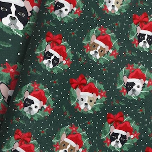 以下が含まれることがあります： サンタ帽とリースをつけたフレンチブルドッグの顔が繰り返されるクリスマス柄の生地。犬たちは様々な毛色をしており、赤いリボンとポインセチアが飾られた濃い緑色の背景です。生地は折りたたまれており、パターンの繰り返しを示しています。