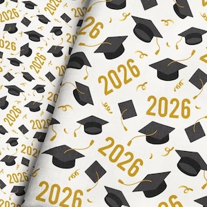 May include: Fabric with a repeating pattern of black graduation caps, squares, and the year "2026" in gold on a white background. The design includes gold confetti-like accents. Ideal for graduation-themed projects.