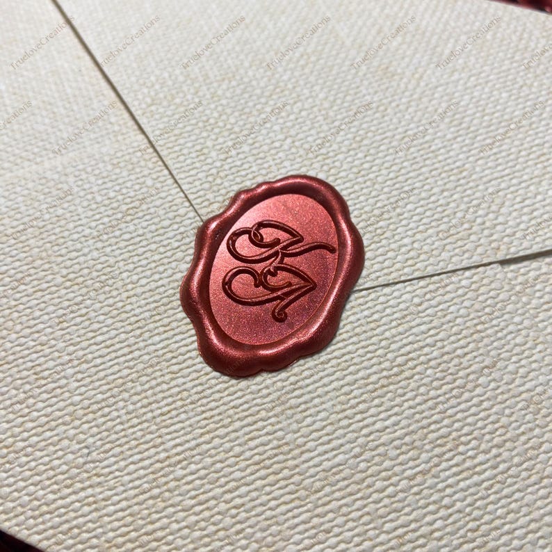 May include: A red wax seal with the initials "BB" on a cream envelope. The oval seal has a textured surface and a metallic sheen. The envelope has a woven texture and a visible seam.