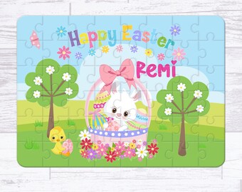 May include: A personalized Easter puzzle featuring a white bunny holding an egg in a pink basket with a pink bow. The puzzle has a blue sky background with green grass and two trees. The text "Happy Easter Remi" is printed on the puzzle.