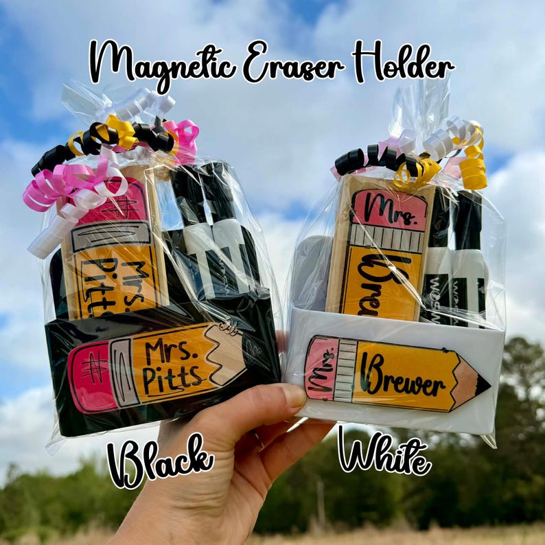 Op de afbeelding: Twee geschenksets, &eacute;&eacute;n zwart en &eacute;&eacute;n wit, elk met een magnetische gumhouder in de vorm van een potlood, met de tekst "Mrs. Pitts" en "Mrs. Brewer". De sets bevatten ook spuitflessen en zijn verpakt in cellofaan met decoratieve linten.