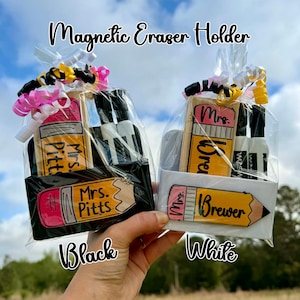 May include: Two gift sets, one black and one white, each containing a magnetic eraser holder shaped like a pencil, with the names "Mrs. Pitts" and "Mrs. Brewer" on them. The sets also include spray bottles and are wrapped in cellophane with decorative ribbons.