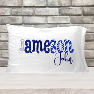 May include: White pillowcase with the name "Jameson John" printed in blue patterned letters.