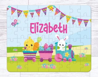 May include: A personalized Easter-themed puzzle featuring a yellow chick and a white bunny riding a train decorated with Easter eggs. The puzzle is on a blue background with a banner of colorful flags and the name "Elizabeth" written in pink.