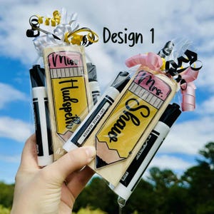 Op de afbeelding: Twee cadeau sets, elk met een potloodvormig item en twee droog uitwisbare markers. E&eacute;n set is gelabeld "Miss Hudspeth" en de andere "Mrs. Shaw". De sets zijn verpakt in doorzichtig cellofaan en vastgebonden met linten.