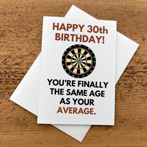 May include: A white greeting card with a brown text header reading HAPPY 30th BIRTHDAY! and a central graphic of a circular dartboard with black, red, green, and white segments. Below the dartboard, black text reads YOU'RE FINALLY THE SAME AGE AS YOUR AVERAGE.