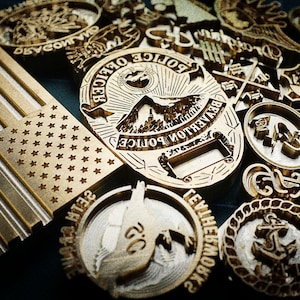 Könnte beinhalten: Eine Sammlung verschiedener Messingstempel, darunter eine stilisierte amerikanische Flagge, Polizeimarken und andere Emblemdesigns. Die Stempel sind in verschiedenen Formen und Größen mit aufwendigen Details.