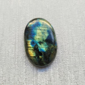 May include: A smooth, oval-shaped labradorite gemstone with iridescent blue, green, and gold colors.