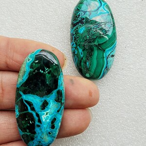 Op de afbeelding: Twee ovale cabochons van turquoise en groene edelsteen. De cabochons hebben een draaiende patroon van turquoise, groen en zwart.