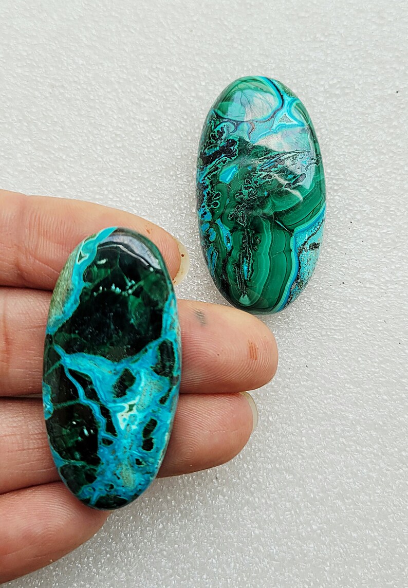 Op de afbeelding: Twee ovale cabochons van turquoise en groene edelsteen. De cabochons hebben een draaiende patroon van turquoise, groen en zwart.