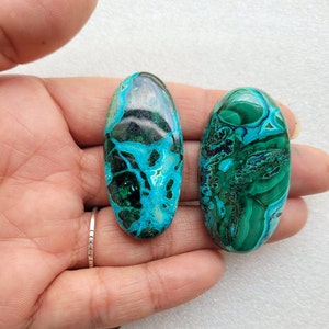 Op de afbeelding: Twee ovale groene en blauwe edelsteen cabochons met een draaiende patroon. De cabochons zijn glad en gepolijst.
