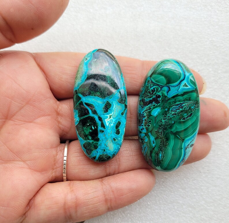 Op de afbeelding: Twee ovale groene en blauwe edelsteen cabochons met een draaiende patroon. De cabochons zijn glad en gepolijst.