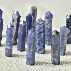 May include: A collection of 14 blue and white sodalite crystal points. The points are arranged in a semi-circle on a white surface.