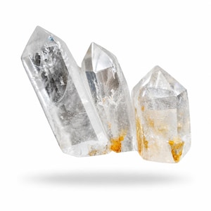 May include: Three clear quartz crystal points with natural inclusions and slight yellow-orange mineral deposits. The crystals are arranged in a cluster, each with a pointed tip. The background is white.