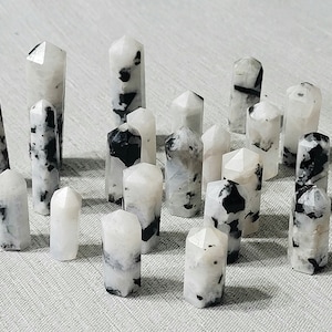 May include: A collection of 18 white and black gemstone points, also known as rainbow moonstone points. The points are arranged in a semi-circle on a white surface.