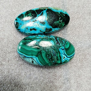 Op de afbeelding: Twee ovale groene en blauwe edelsteen cabochons. De stenen hebben een draaiende patroon van groen, blauw en zwart.