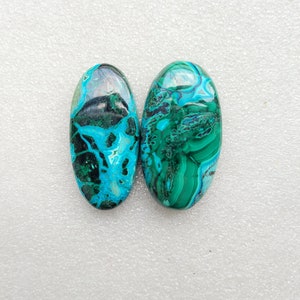 Op de afbeelding: Twee ovale cabochons van groene en blauwe chrysocolla. De stenen hebben een draaiende patroon van groen, blauw en zwart.