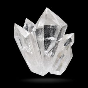 May include: A cluster of clear quartz crystals with sharp, pointed terminations. The crystals are translucent, allowing light to pass through, and are set against a black background. The overall shape is a natural, irregular formation.