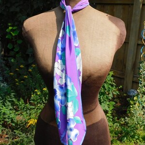 May include: A purple and blue floral patterned scarf with white flowers. The scarf is tied around a brown dress form.