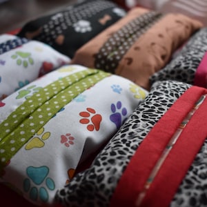 May include: A collection of rectangular fabric tissue holders featuring various patterns including colourful paw prints on white, black with white paw prints, solid tan, and black and white animal print with solid coloured fabric centre strips.