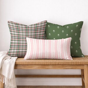 May include: Three decorative throw pillows on a wooden bench. One pillow has a green and pink plaid pattern, another is green with a white floral design, and the third is pink and white striped.