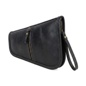 May include: Black leather clutch bag with a curved design. Features a vertical zip and a wrist strap. The bag has dark grey stitching and a bronze-coloured zip.