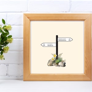 Könnte beinhalten: Ein gerahmter Druck eines Wegweisers mit zwei Richtungspfeilen. Der obere Pfeil zeigt nach "Ballyshannon" und der untere Pfeil zeigt nach "Bundoran". Der Wegweiser ist von grünen Pflanzen und Blumen umgeben.