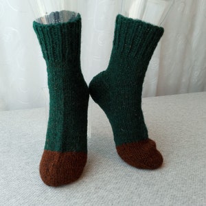 May include: A pair of green knitted socks with brown toes. The socks are on a white surface.
