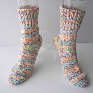 May include: A pair of colorful knitted socks. The socks feature a mix of pastel colors including yellow, pink, blue, and green. The cuff of the socks is ribbed, and the body of the socks has a textured knit pattern.