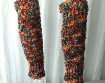 May include: A pair of colorful knitted leg warmers. The leg warmers are a mix of red, orange, green, and blue yarns. The cuffs and edges have a textured, looped design. The leg warmers are displayed on clear mannequins against a white background.