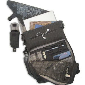 May include: A gray canvas messenger bag with a laptop, water bottle, phone, and other accessories inside. The bag has a zippered pocket and a mesh pocket. The bag is open and the contents are visible.