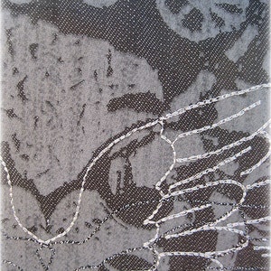 May include: A close-up of a gray fabric with a white embroidered design. The embroidery is in the shape of a bird's wing.
