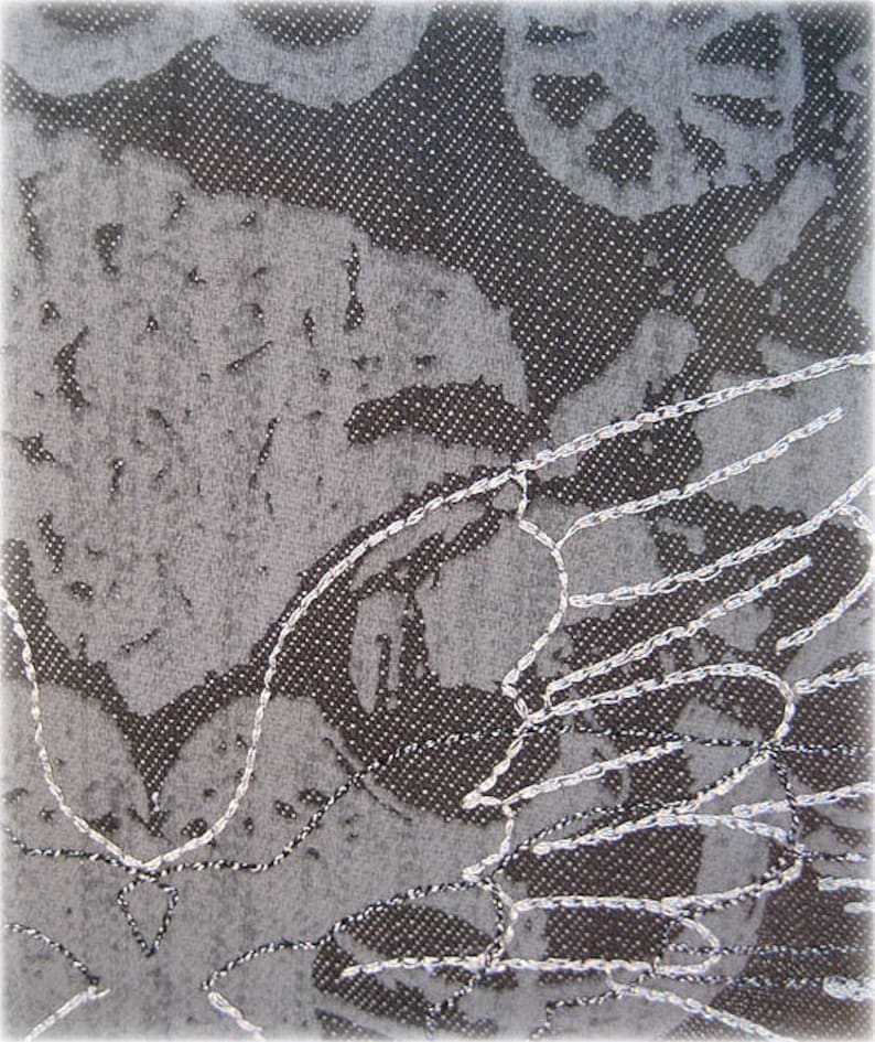 May include: A close-up of a gray fabric with a white embroidered design. The embroidery is in the shape of a bird's wing.