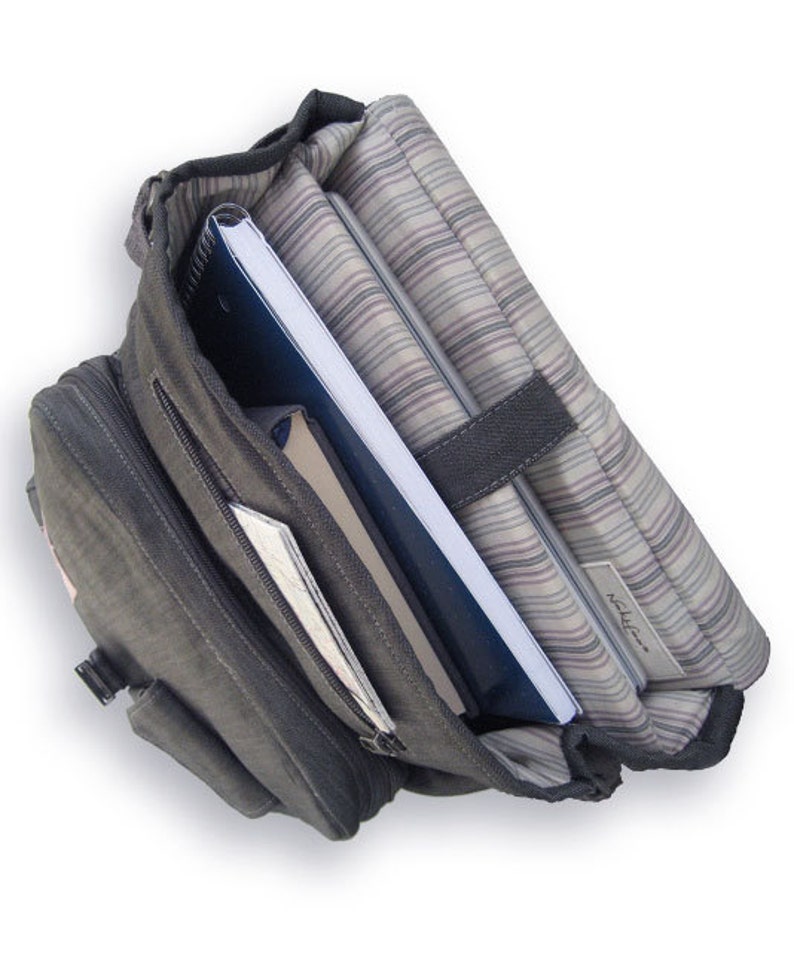 May include: A gray canvas backpack with a zippered pocket and a laptop compartment. The backpack is open and contains a blue notebook, a brown notebook, and a silver laptop.