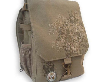 May include: A tan backpack with a flap closure and a dragon design embroidered on the front. The backpack has a side mesh pocket, adjustable straps, and a small patch with a star and wings. The bag is made of a durable material and features metal hardware.