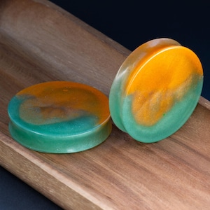 May include: A pair of green and orange resin ear gauges. The gauges have a swirling pattern of green and orange.