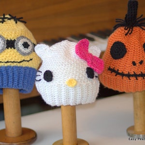 May include: Three crocheted hats, one yellow and blue with a minion face, one white with a Hello Kitty face and a pink bow, and one orange with a jack-o'-lantern face.