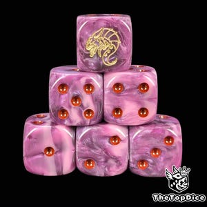 Puede incluir: Un conjunto de seis dados apilados, con un patrón arremolinado rosa y morado. El dado superior presenta un dragón dorado. Cada dado tiene puntos naranjas. Para juegos de mesa.