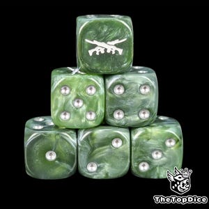 May include: A stack of six green dice with a marbled effect. The top die features a white crossed-rifle design. Each die has silver pips. The dice are arranged against a black background.