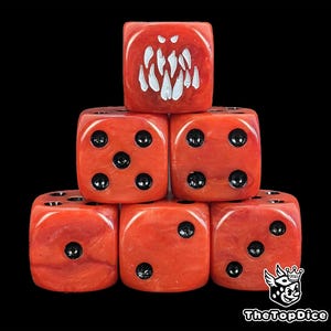 May include: A stack of six red dice with black pips. One die features a white, jagged design resembling teeth. The dice are arranged against a black background. The logo "TheTopDice" is visible in the bottom right corner.