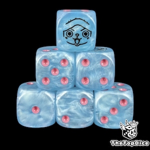 Op de afbeelding: Zes blauwe dobbelstenen met roze ogen zijn gestapeld tegen een zwarte achtergrond. Eén dobbelsteen heeft een zwart cartoongezicht. De dobbelstenen hebben een parelmoer afwerking. Het logo "TheTopDice" staat rechtsonder. Voor bordspellen.