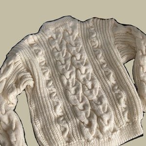 May include: A cream-colored cable knit sweater with a high neck and long sleeves.