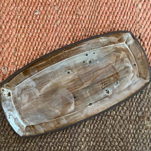 Puede incluir: Bandeja rectangular de cerámica con un diseño veteado marrón y blanco. La bandeja tiene un borde marrón oscuro y un borde ligeramente elevado. La superficie tiene pequeñas motas oscuras. Ideal para servir aperitivos o exhibir objetos decorativos.