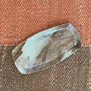 Puede incluir: Plato rectangular de cerámica con un diseño veteado en verde claro y marrón. El plato tiene un borde ligeramente elevado y está sobre un fondo texturizado de dos tonos naranja y marrón.