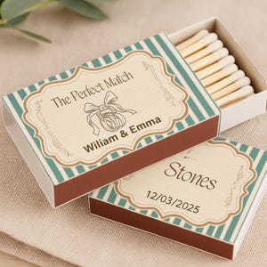 Könnte beinhalten: Eine dekorative Streichholzschachtel mit einem türkis-braunen Streifendesign. Die Schachtel trägt den Text "The Perfect Match" und die Namen "William & Emma". Die Schachtel enthält Holzstreichhölzer.
