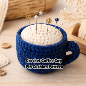 May include: A dark blue crochet coffee cup pin cushion with a cream-coloured top, featuring six decorative pins with various metal and pearl-like heads. The text Crochet Coffee Cup Pin Cushion Pattern is printed in white over the front of the cup.