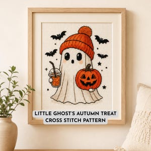 May include: A framed cross stitch pattern titled LITTLE GHOST'S AUTUMN TREAT. The design features a white ghost wearing an orange knit hat, holding an orange drink in a clear cup and a carved jack-o'-lantern pumpkin, surrounded by black bats.