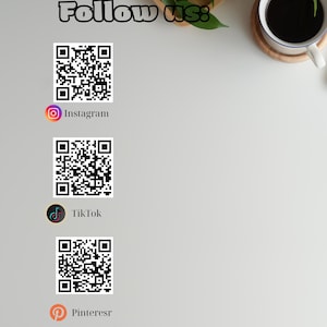 May include: White background with the text "Follow us:" in a handwritten style. Below are QR codes for Instagram, TikTok, and Pinterest, each with its respective logo. A cup of coffee sits on a coaster in the upper right corner.