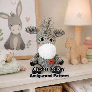 May include: A gray crocheted donkey amigurumi toy with a white muzzle, black hooves, and a small red heart-shaped button on its chest. The text Crochet Donkey Amigurumi Pattern is displayed in black letters at the bottom of the toy.