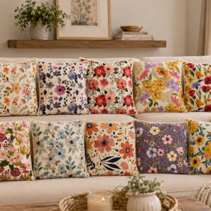 May include: A collection of square throw cushions featuring various floral patterns in vibrant colours including red, yellow, blue, purple, and orange. Each cushion has a textured fabric surface with detailed botanical prints of flowers and leaves.
